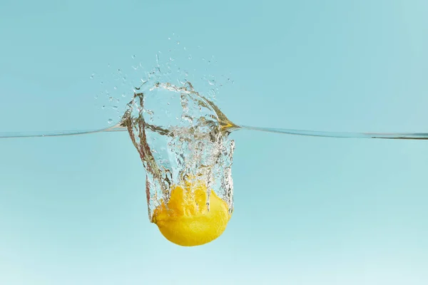 Frische gelbe Zitrone fällt tief ins Wasser mit Spritzer auf blauem Hintergrund — Stockfoto