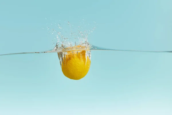 Zitrone fällt tief ins Wasser mit Spritzer auf blauem Hintergrund — Stockfoto