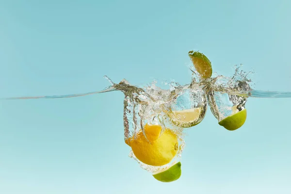 Reife Zitrone und geschnittene Limette tief ins Wasser fallen mit Spritzer auf blauem Hintergrund — Stockfoto