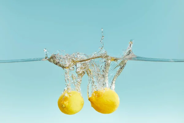 Whole lemons falling deep in water with splash on blue background — Stock Photo