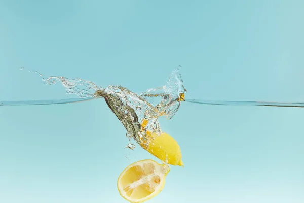 Limones cortados que caen profundamente en el agua con salpicaduras sobre fondo azul - foto de stock