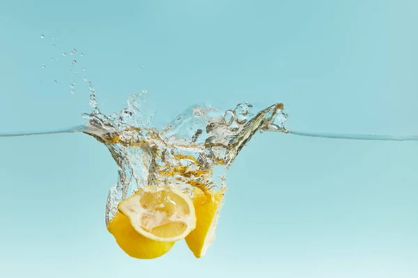 Gelbe reife Zitronen fallen tief ins Wasser mit Spritzer auf blauem Hintergrund — Stockfoto