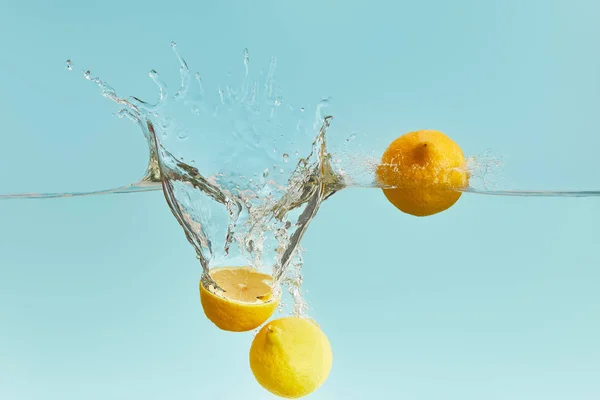 Frische reife Zitronen fallen tief ins Wasser mit Spritzer auf blauem Hintergrund — Stockfoto