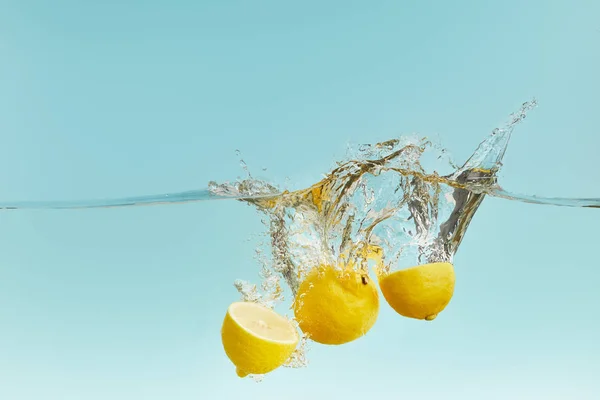 Frische Zitronen fallen tief ins Wasser mit Spritzer auf blauem Hintergrund — Stockfoto