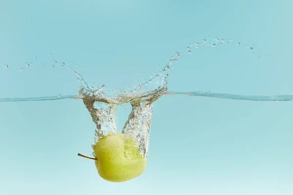 Pomme verte mûre tombant profondément dans l'eau avec éclaboussure sur fond bleu — Photo de stock