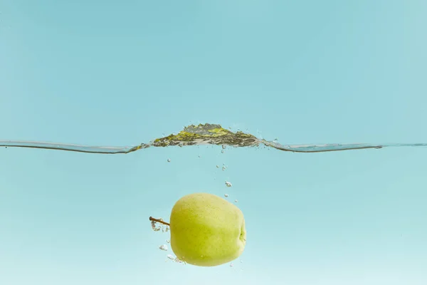 Maçã verde na água com bolhas no fundo azul — Fotografia de Stock