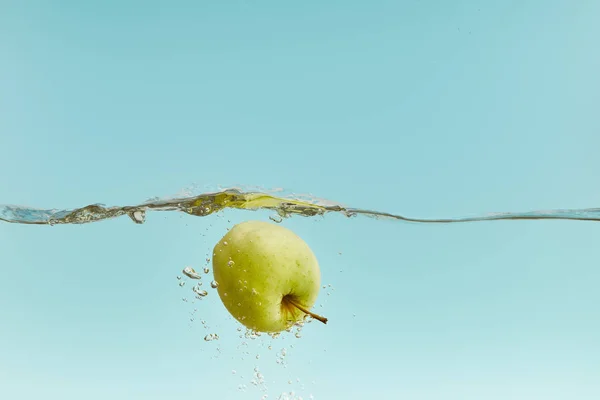 Свежее зеленое яблоко в воде с пузырьками на голубом фоне — стоковое фото