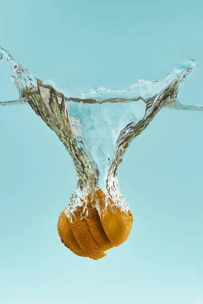 Couper kiwi tomber profondément dans l'eau avec éclaboussure sur fond bleu — Photo de stock