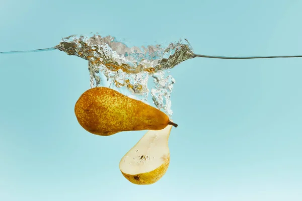 Cut pear falling deep in water with splash on blue background — Stock Photo