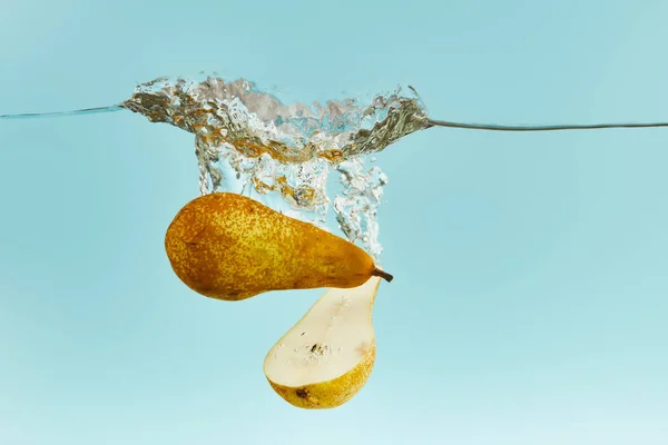 Geschnittene Birne fällt tief ins Wasser mit Spritzer auf blauem Hintergrund — Stockfoto