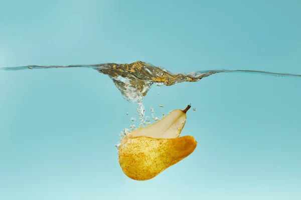 Reife Birnenhälften fallen tief ins Wasser mit Spritzer auf blauem Hintergrund — Stockfoto