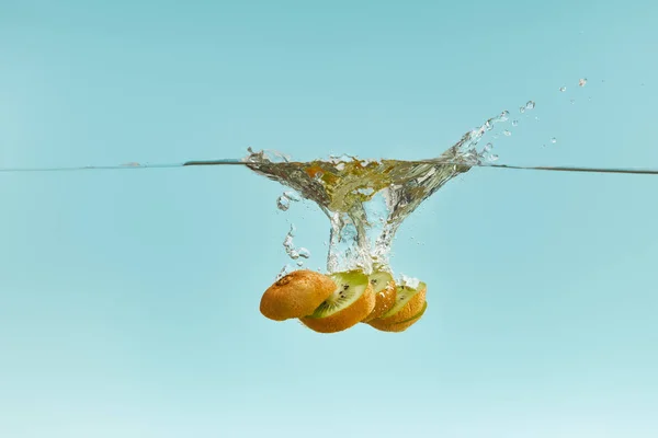 Ripe kiwi slices falling deep in water with splash on blue background — Stock Photo