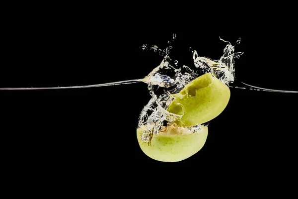 Manzana verde cortada que cae profundamente en el agua con salpicadura aislada en negro - foto de stock