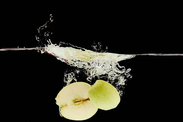 Verde manzana mitades cayendo profundamente en el agua con salpicadura aislado en negro - foto de stock