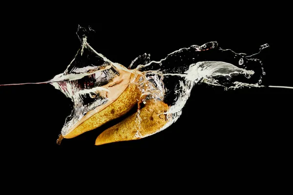 Mitades de pera que caen profundamente en el agua con salpicaduras aisladas en negro - foto de stock