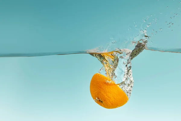 Leuchtend orangefarbene Hälfte fällt ins Wasser mit Spritzer auf blauem Hintergrund — Stockfoto