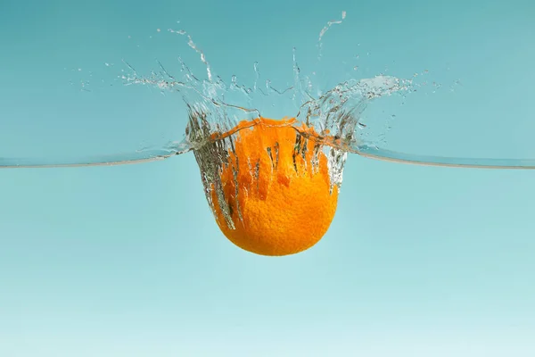 Arancio fresco che cade in acqua con spruzzi su fondo blu — Foto stock