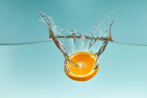 Moitié orange fraîche tombant dans l'eau avec éclaboussure sur fond bleu — Photo de stock