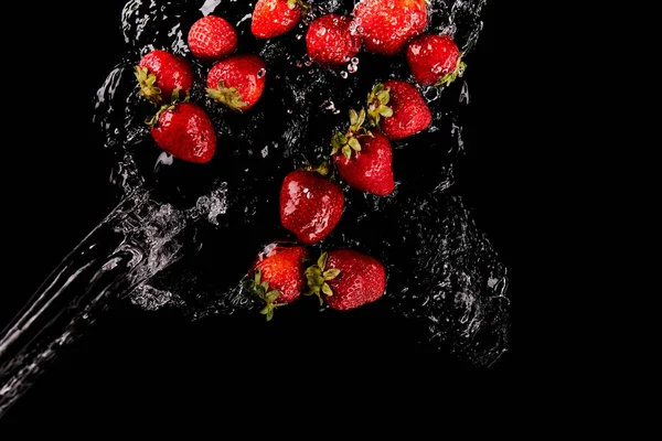 Vue de dessus des fraises rouges mûres avec éclaboussures d'eau isolées sur noir — Photo de stock