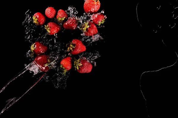 Vue de dessus des fraises rouges mûres avec éclaboussure d'eau claire isolée sur noir — Photo de stock