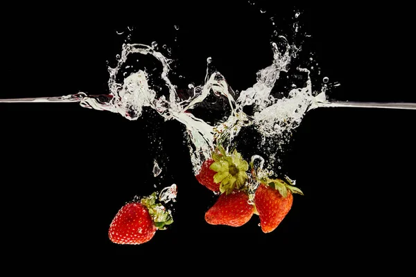Стигла полуниця падає у воду з бризкою ізольовано на чорному — стокове фото