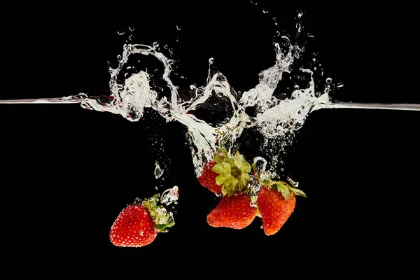 Fraises mûres tombant dans l'eau avec éclaboussures isolées sur noir — Photo de stock