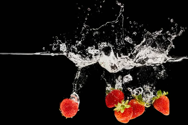 Fraises fraîches mûres tombant dans l'eau avec éclaboussures isolées sur noir — Photo de stock