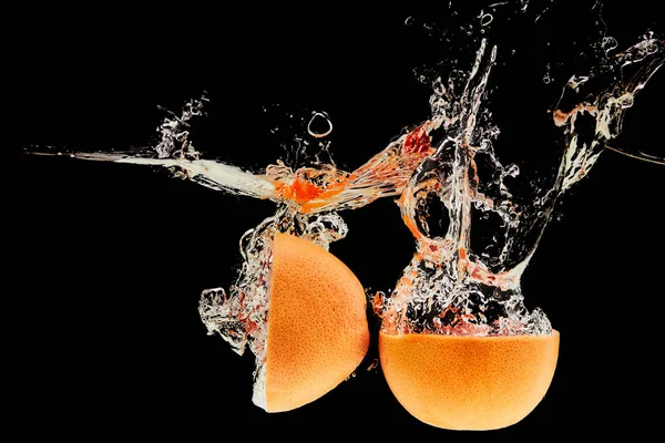 Metà pompelmo cadere in acqua con spruzzi isolati su nero — Foto stock