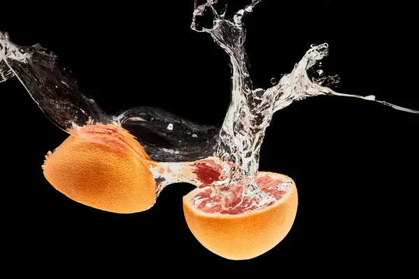 Ripe grapefruit halves falling in water with wave isolated on black — Stock Photo