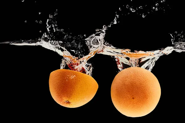 Mitades de pomelo fresco que caen en el agua con salpicaduras aisladas en negro - foto de stock