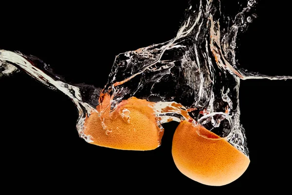 Metades de toranja orgânica caindo na água com respingo isolado em preto — Fotografia de Stock