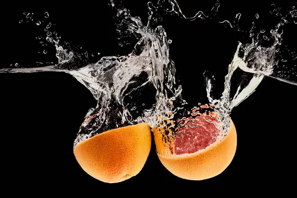 Ripe natural grapefruit halves falling in water with splash isolated on black — Stock Photo