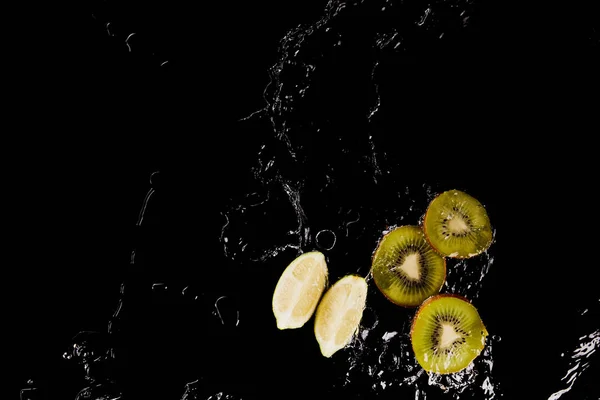 Vue du dessus du citron et du kiwi coupés dans une flaque d'eau claire isolée sur du noir — Photo de stock