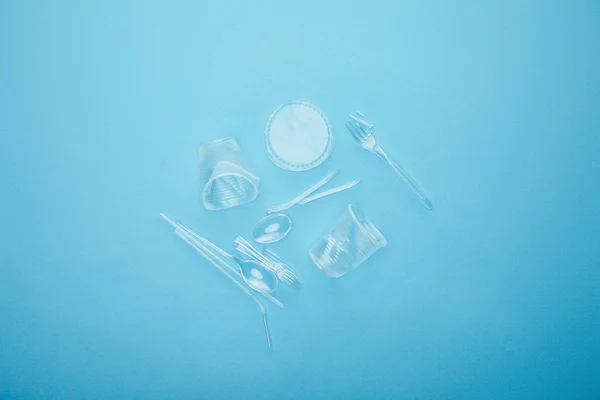 Top view of pile of transparent disposable cups, forks and spoons on blue background — Stock Photo