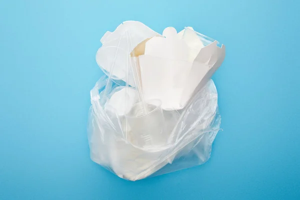 Vue du dessus du sac en plastique avec des tasses et des conteneurs jetables sur fond bleu — Photo de stock