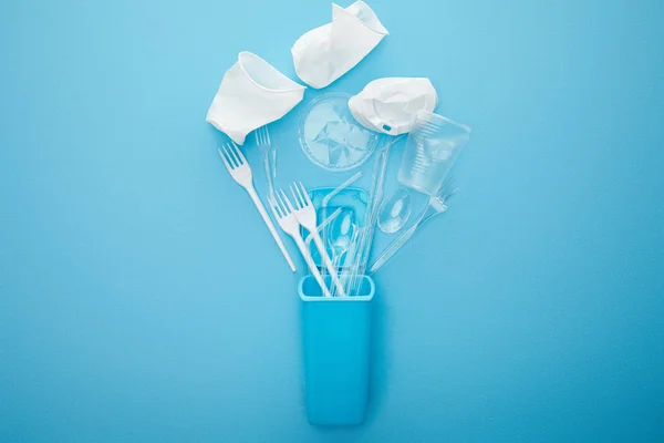 Top view of crumpled plastic cups, forks and spoons near recycle bin on blue background — Stock Photo