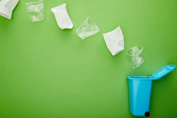 Top view of crumpled plastic cups near blue recycle bin on green background — Stock Photo