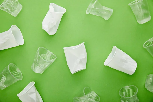 Vista dall'alto di bicchieri di plastica bianco e trasparente monouso su sfondo verde — Foto stock