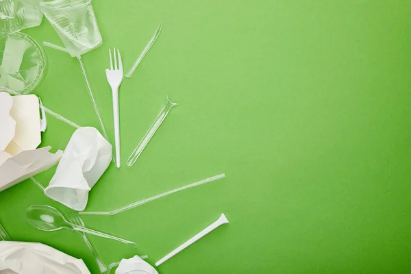 Vista superior de copos de plástico descartáveis, garfos, colheres e recipientes de papelão em fundo verde — Fotografia de Stock
