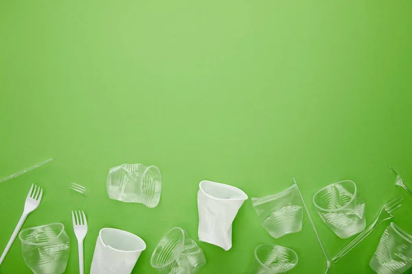 Draufsicht auf zerknüllte Plastikbecher und -gabeln auf grünem Hintergrund mit Kopierraum — Stockfoto