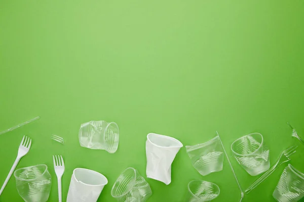Vista superior de copas y tenedores de plástico arrugados sobre fondo verde con espacio para copiar — Stock Photo