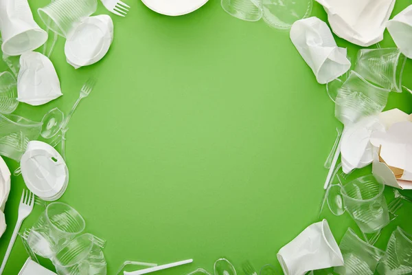 Top view of crumpled plastic cups, forks, plates and cardboard container on green background with copy space — Stock Photo