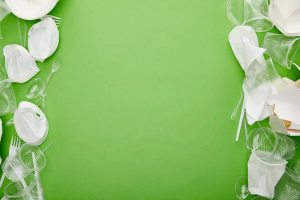 Vista dall'alto di bicchieri di plastica accartocciati e contenitore di cartone su sfondo verde con spazio di copia — Foto stock