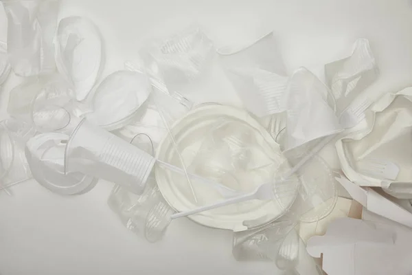 Vista dall'alto di bicchieri di plastica accartocciati, piatti e contenitore di cartone su sfondo bianco — Foto stock