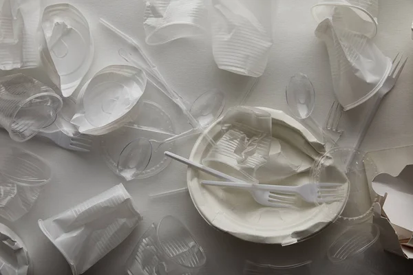 Вид сверху на скомканные одноразовые тарелки, пластиковые чашки, вилки и ложки на белом фоне — стоковое фото