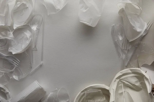 Вид сверху на скомканные одноразовые тарелки, пластиковые чашки, вилки и ложки на белом фоне с копировальным пространством — стоковое фото