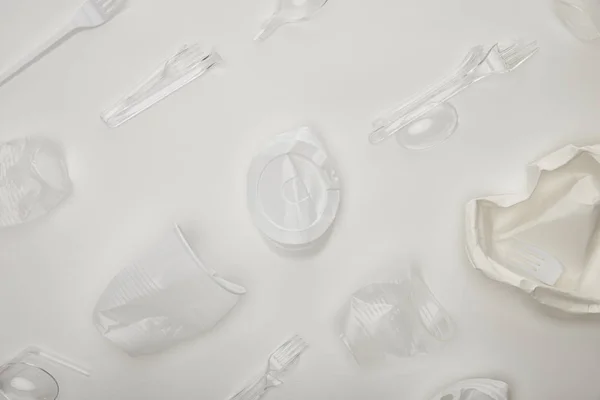 Vista superior de copos crumpled descartáveis, garfos, colheres e placa no fundo branco — Fotografia de Stock