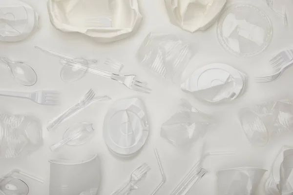 Вид сверху на скомканные одноразовые чашки, вилки, ложки и тарелки на белом фоне — стоковое фото