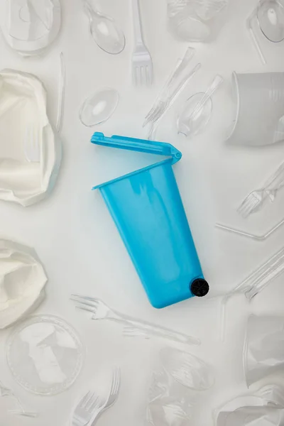 Vista superior de la papelera de reciclaje azul, vasos desechables arrugados, tenedores, cucharas y placa sobre fondo blanco - foto de stock