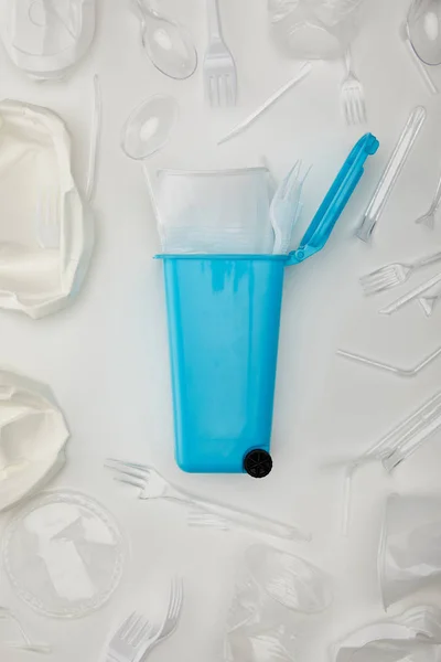 Vista superior de la papelera de reciclaje azul con taza desechable arrugada, tenedor, cucharas y platos sobre fondo blanco - foto de stock